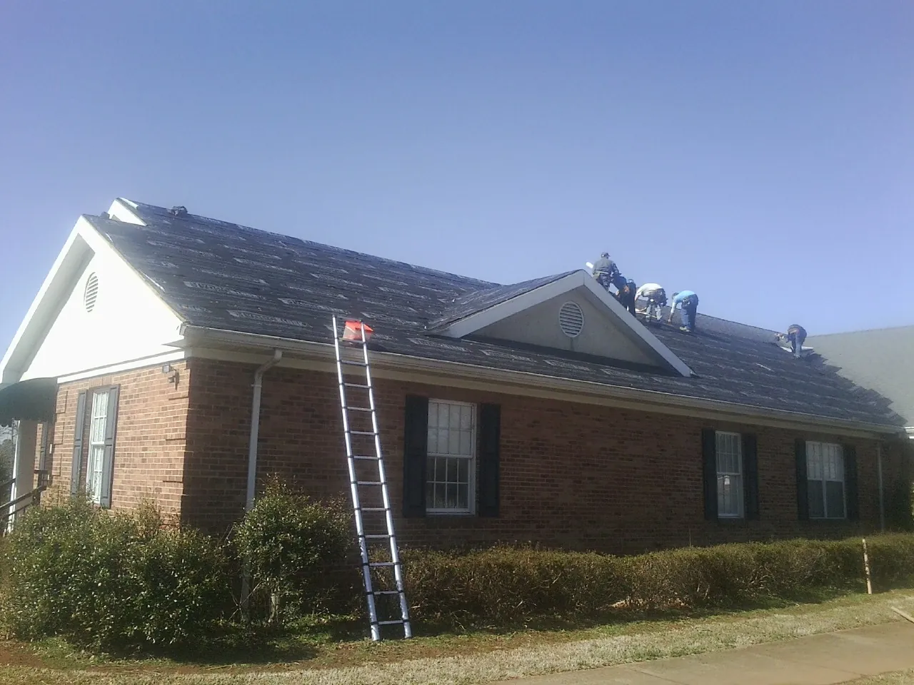 Crew tearing shingles off a brick ranch roof with a ladder set — Emergency Roof Repair work by our crew in Santee