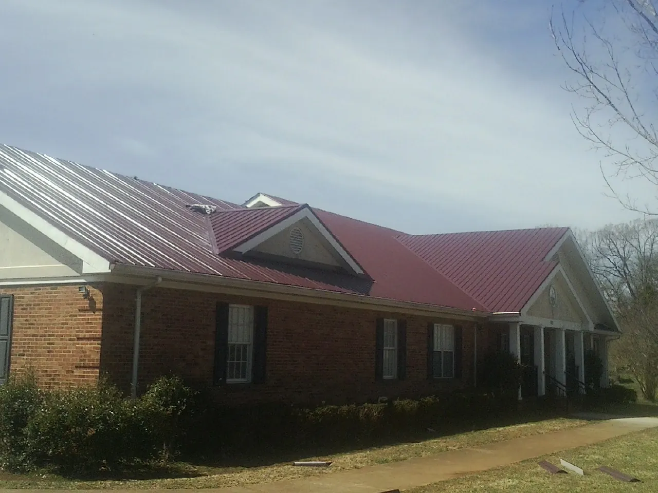Red metal roof with gabled entries on a long brick building, from a Hail Damage Roof Repair job in Santee